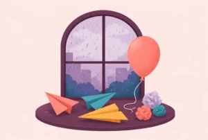 Paper airplanes, a balloon and paper balls on a table by a rainy window